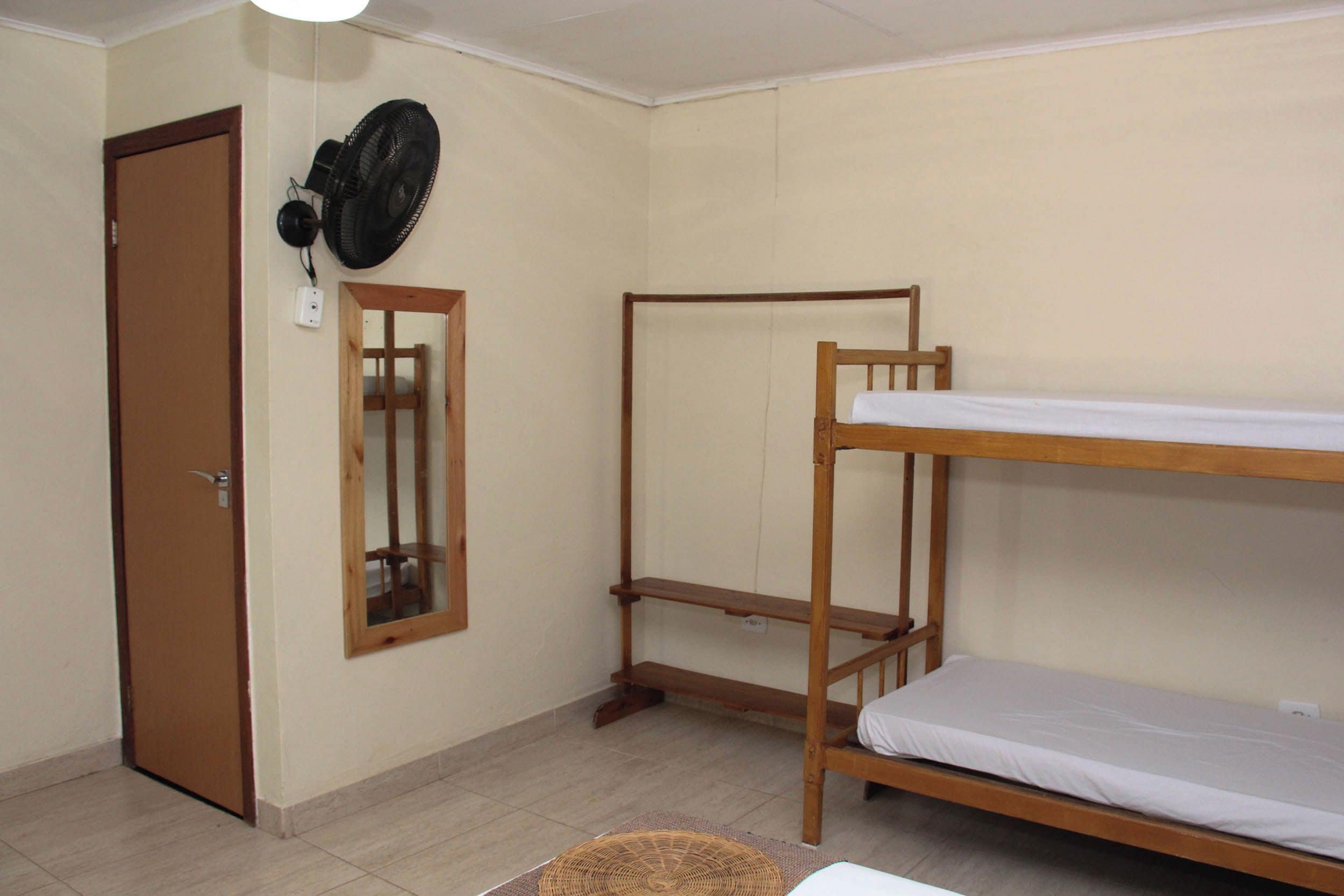 A room with a bunk bed, a mirror, a door, and a standing fan.