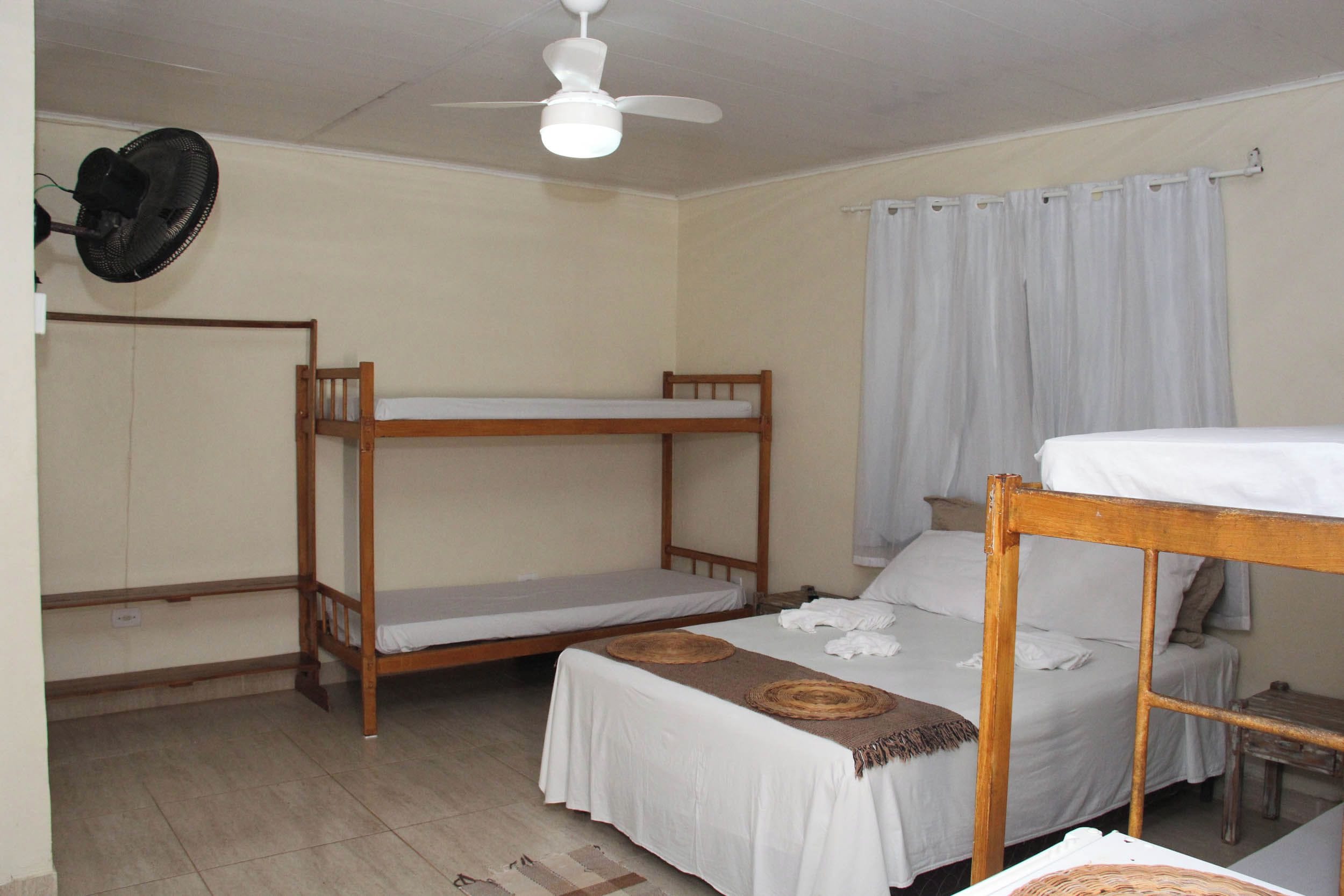 A room with bunk beds, a ceiling fan, a window with curtains, and a small table.