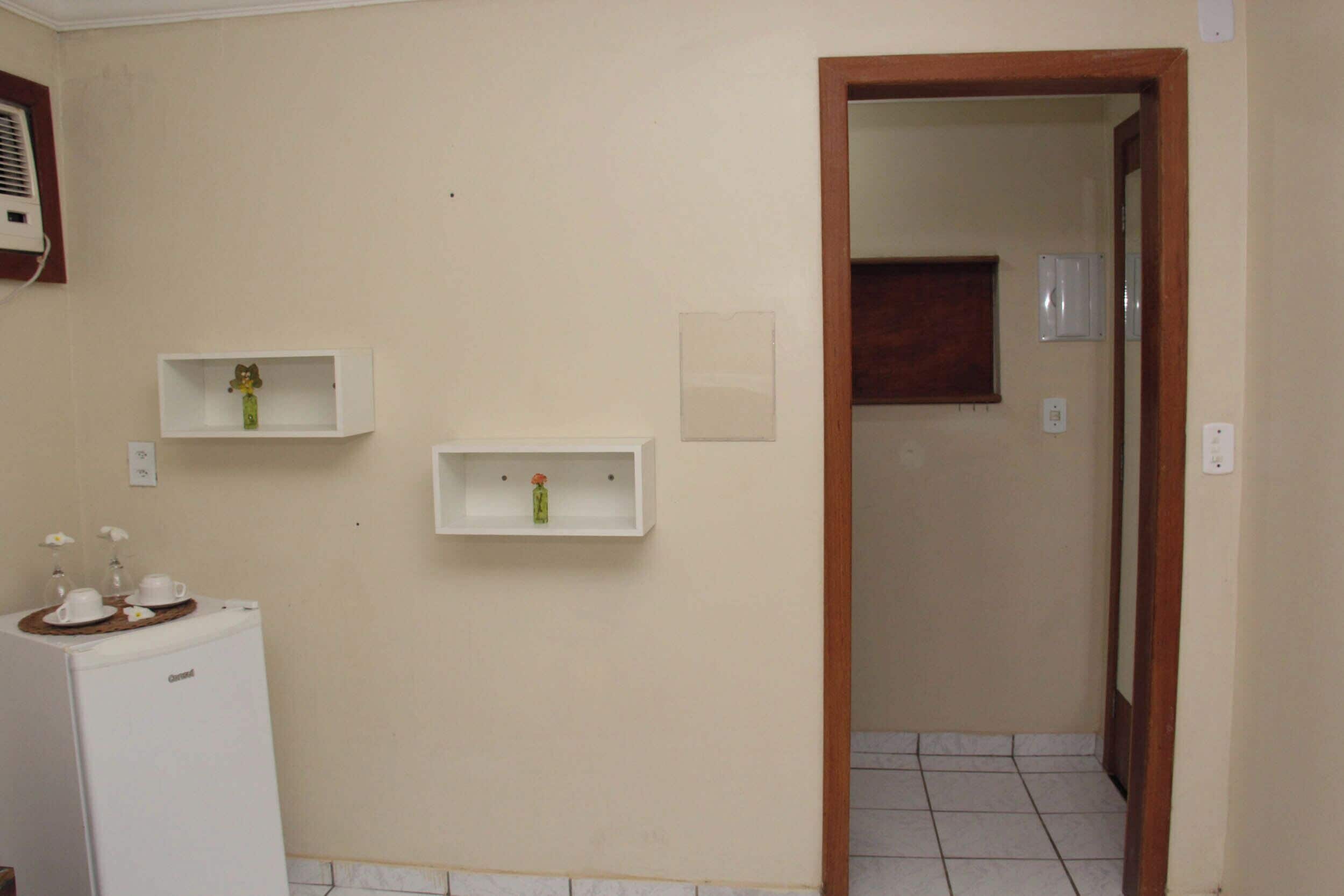 A bathroom with a white refrigerator, two wall-mounted shelves with vases, and a tiled floor.
