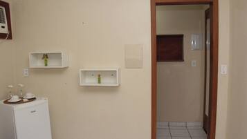 A bathroom with a white refrigerator, two wall-mounted shelves with vases, and a tiled floor.