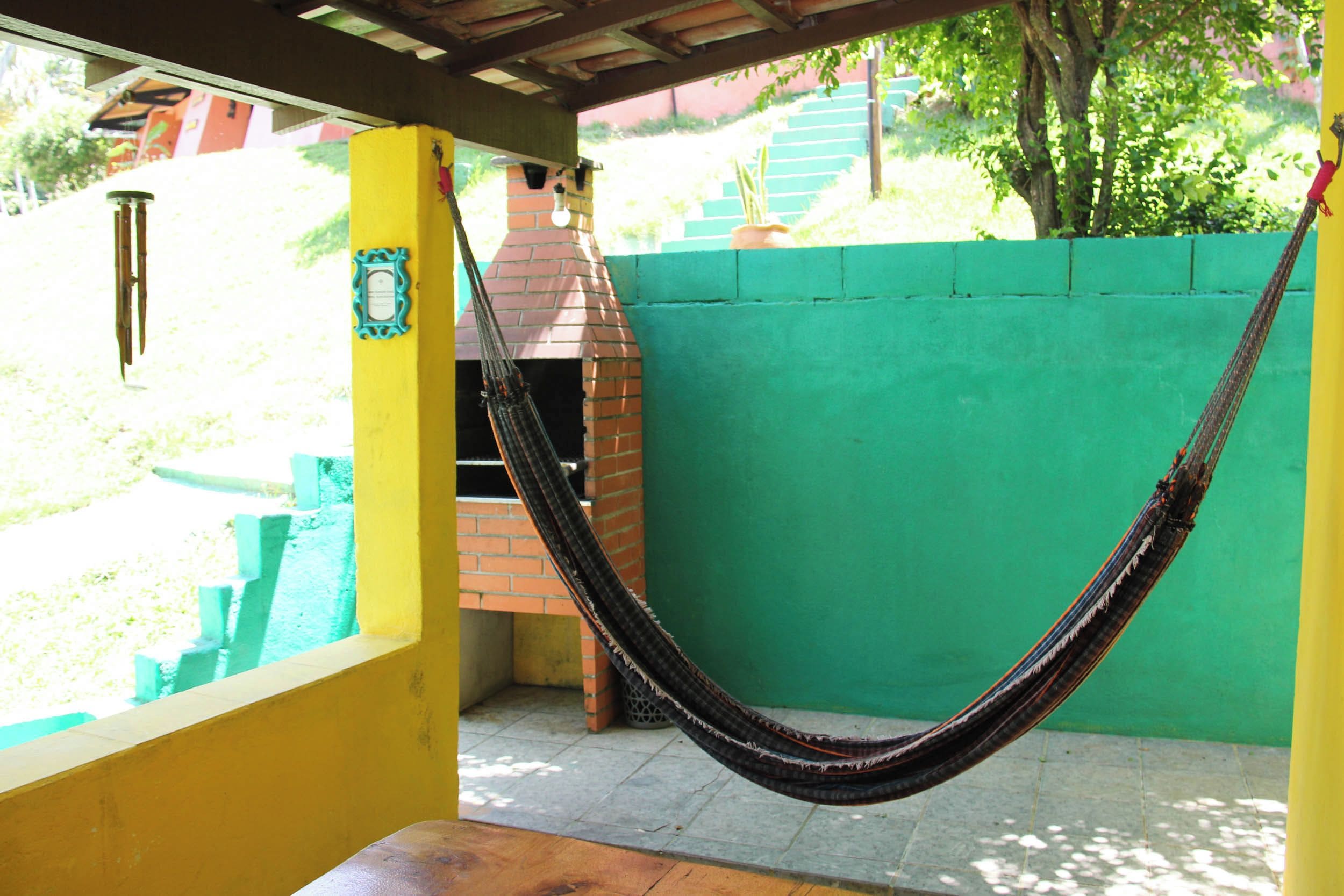 A hammock hanging between yellow and green walls, a brick oven, and a window overlooking a yard.
