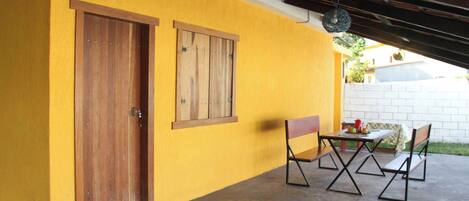 Un bâtiment jaune avec une porte et une fenêtre en bois, une table avec des chaises et un luminaire suspendu.