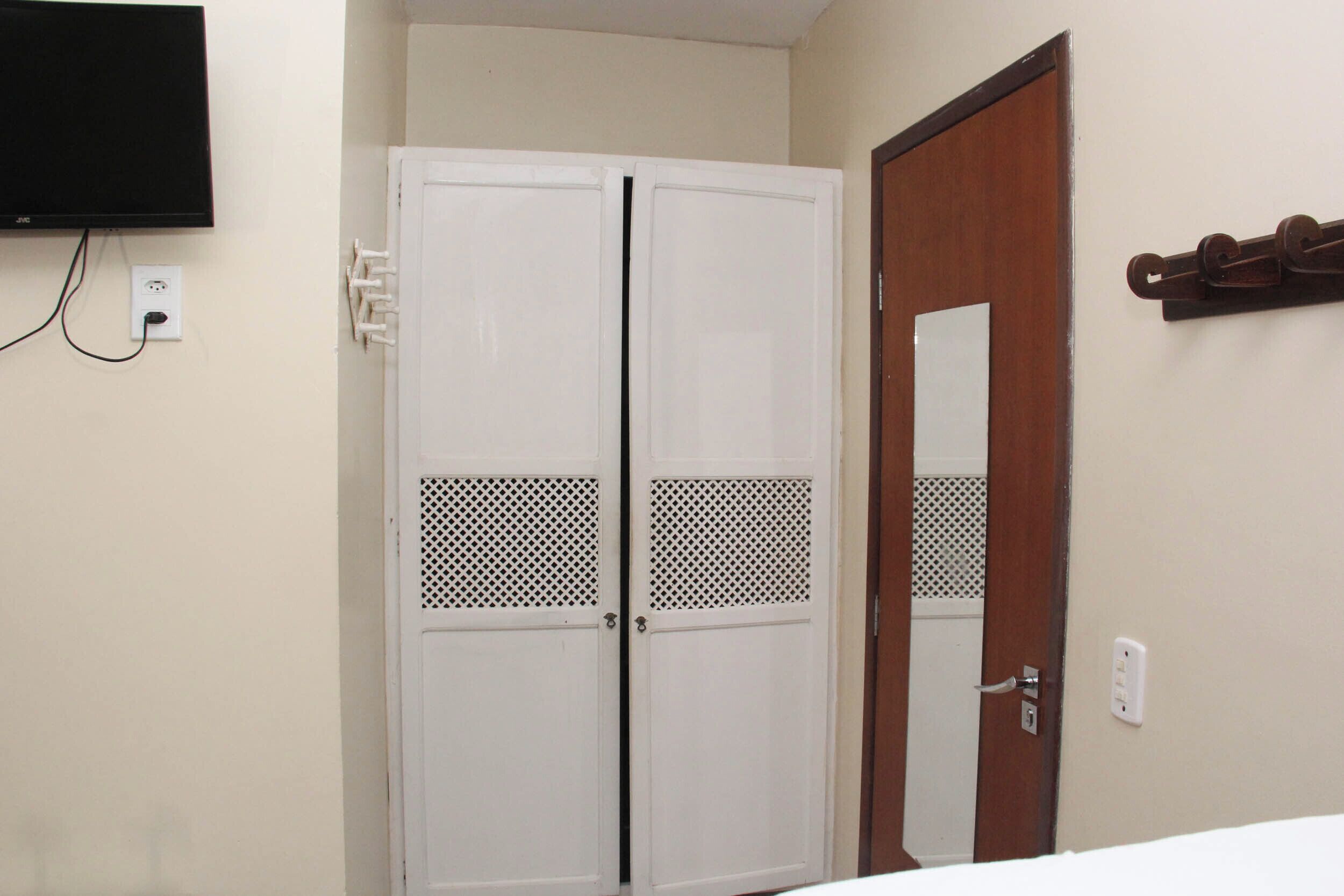 Una habitación con un armario blanco, una puerta de madera y un televisor montado.