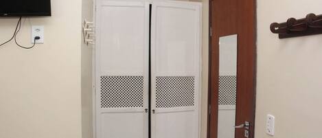 Una habitación con un armario blanco, una puerta de madera y un televisor montado.