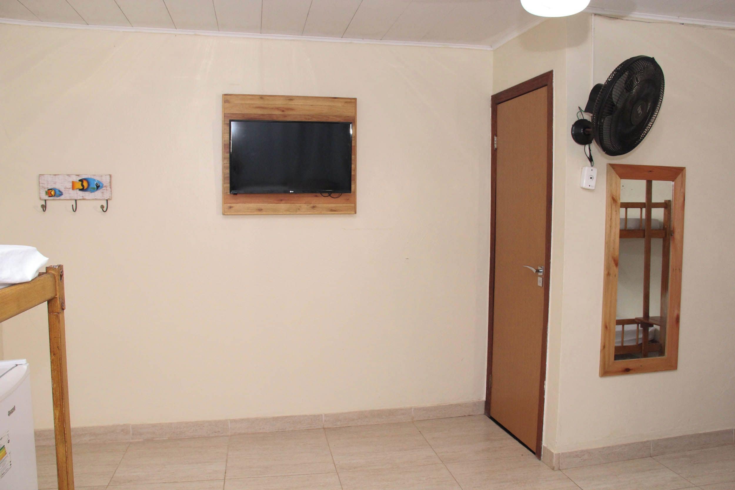 A room with a wooden door, a small window, a wall-mounted fan, and a shelf with decorative items.