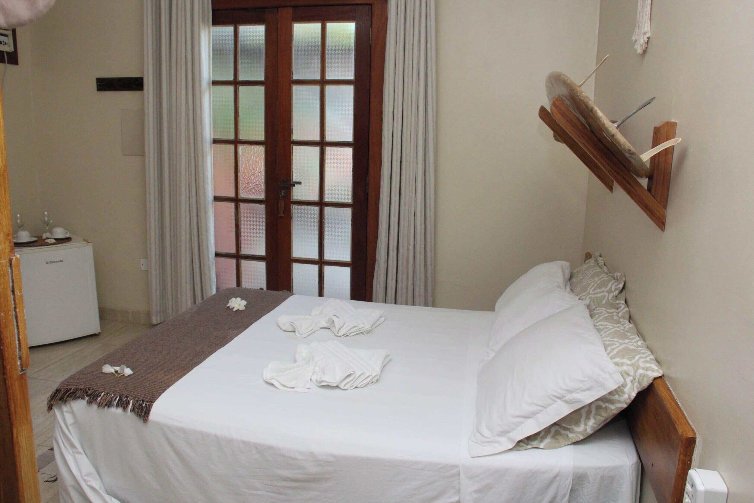 A neatly made bed with white linens and towels, a wooden headboard, and a small bedside table with a lamp.