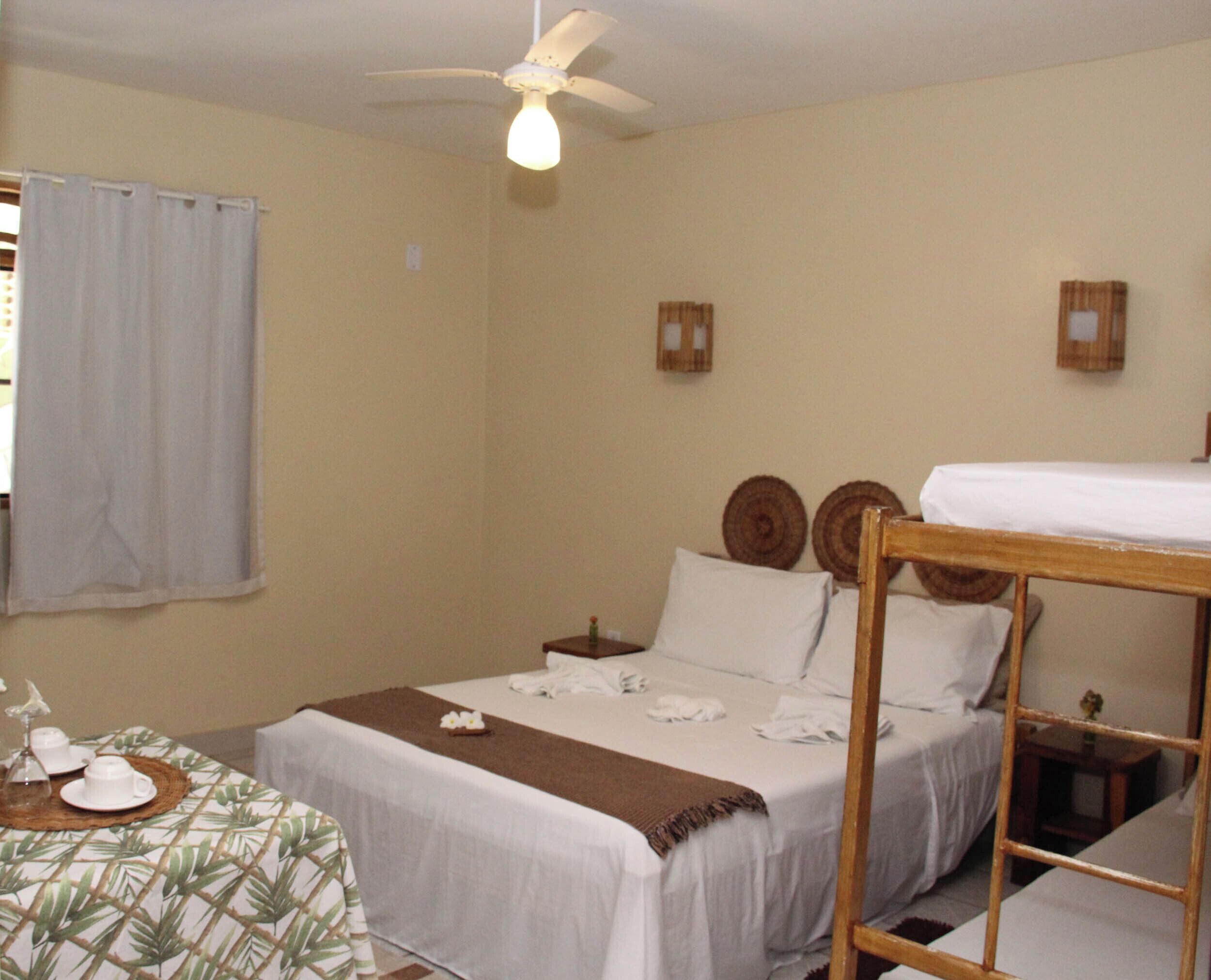 Quarto de hotel com duas camas, um ventilador de teto e uma mesa com toalha e um vaso de flores.