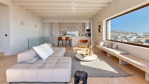 A modern living room with a sofa, a coffee table, and a view of a cityscape through a large window. - Villa in Mykonos with 10 bedrooms sleeps 20 (Mykonos)