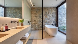 Un bany modern amb una paret de pedra, una banyera gran i un lavabo amb mirall i dos rentabios.