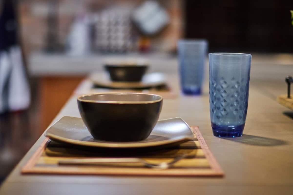 A table set with a dark bowl, a blue glass, and a plate on a placemat.