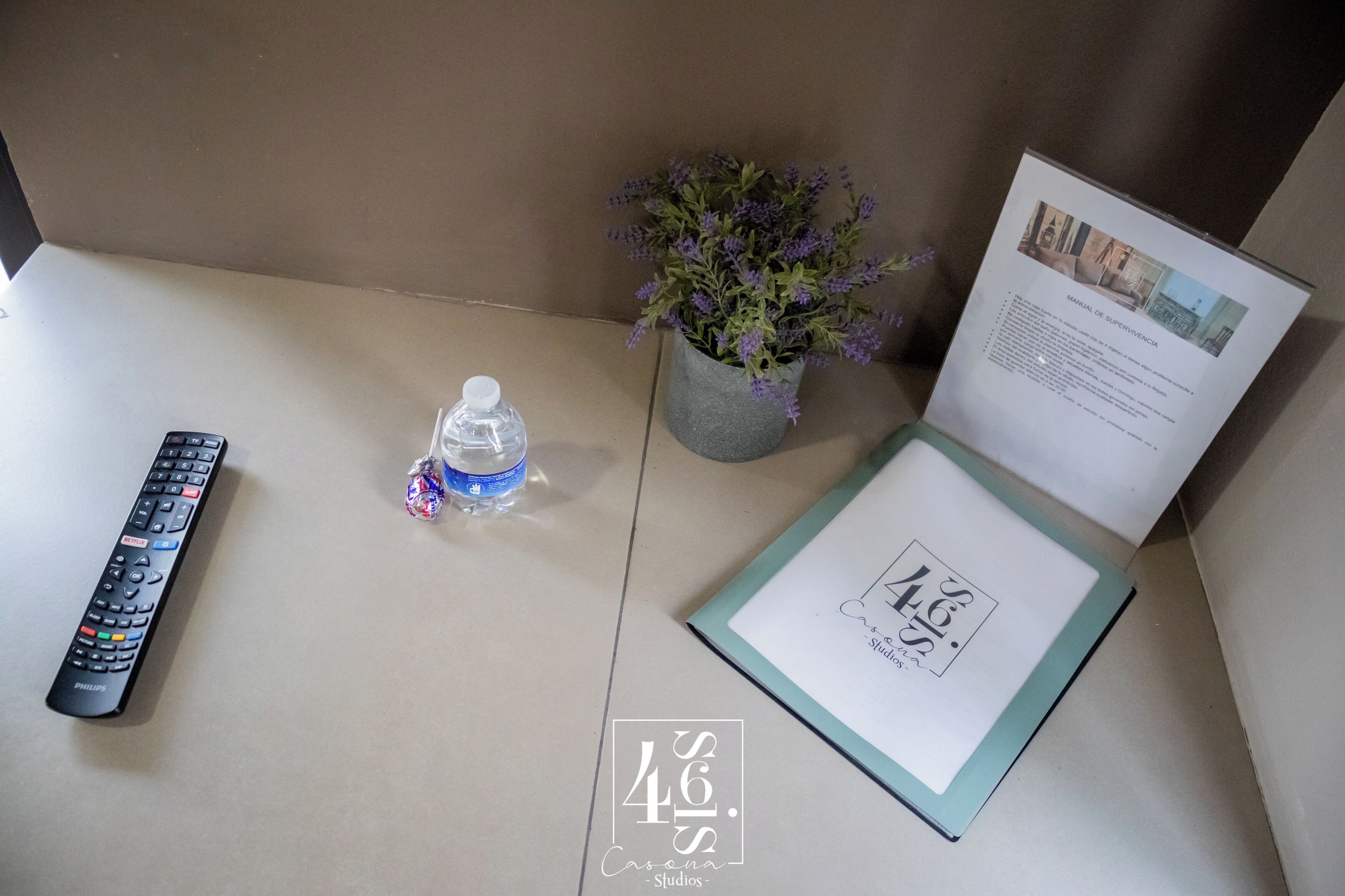Un control remoto, una botella de agua, una planta en maceta y un certificado enmarcado sobre una mesa.