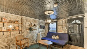 Un salón acogedor con pared de ladrillo, un sofá azul, una silla de madera, una mesita y un ventilador de techo.