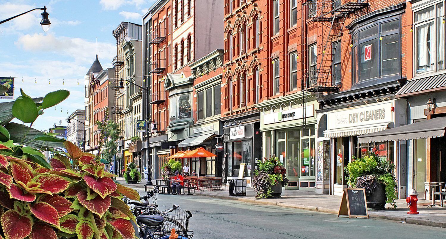 A street lined with historic buildings, a cafe with outdoor seating, and a dry cleaners.