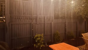 Una cerca de madera con luces de cuerda, una pequeña mesa y una silla en un jardín.