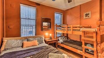 A room with a bunk bed, a single bed, a desk with a lamp, and a window with blinds.