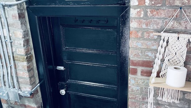 Una puerta negra con un letrero que dice "MY HAPPY PLACE" sobre ella, frente a un muro de ladrillo.