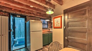 Una cocina compacta con refrigerador, una mesa de comedor con sillas, piso de madera y una puerta con un letrero que indica el baño.