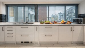 A modern kitchen with a large window, white cabinets, and a stainless steel sink. - The George Street Residences (London)