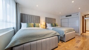 A modern hotel room with two beds, a large window with sheer curtains, and a wooden floor. - The George Street Residences (London)