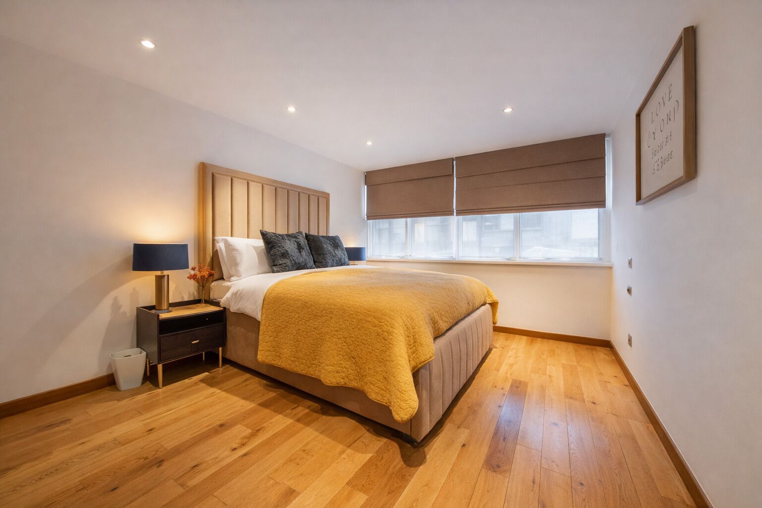 Un dormitorio con cama, mesita de noche, lámpara y ventana con persianas.