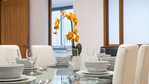 A dining table set with white plates, bowls, and wine glasses, accompanied by a vase of yellow orchids. - The George Street Residences (London)
