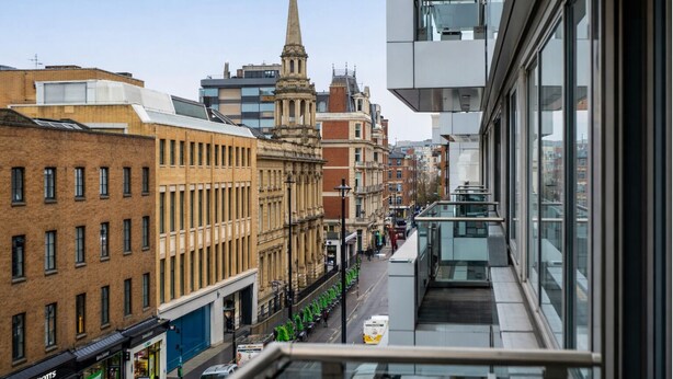 A view from a high-rise building overlooking a street with historic buildings, a church spire, and modern architecture. - The George Street Residences (London)