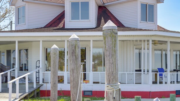 Een huis met twee verdiepingen, een overdekte veranda, houten pilaren en rood-witte details.