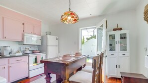 Een keuken met roze kastjes, een houten eettafel en een lamp met gebrandschilderd glas.