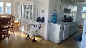 A modern kitchen with white cabinetry, a large water dispenser, and a dining area with wooden chairs and a table.