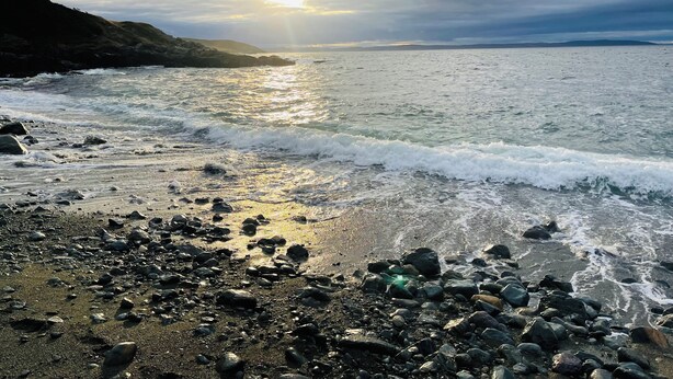A rocky beach with waves crashing onto the shore and a sunset in the background.