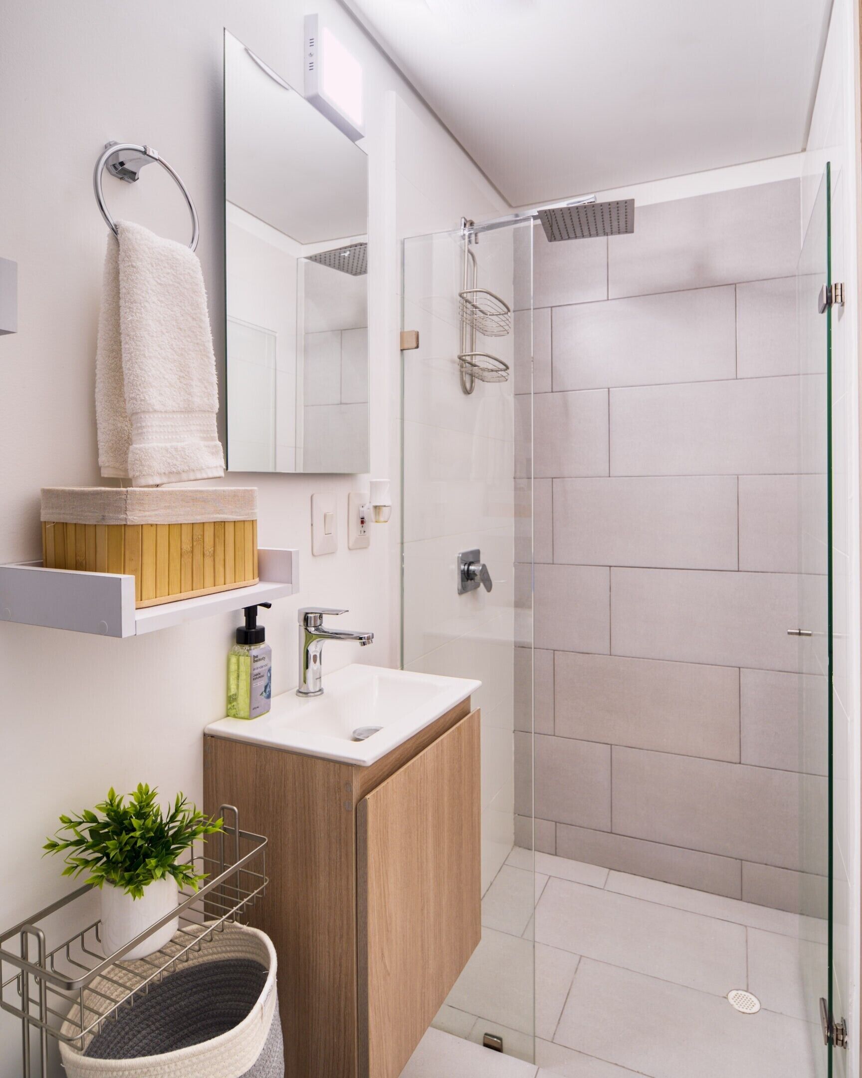 A modern bathroom with a glass shower enclosure, a wooden vanity, a mirror, and a towel rack.