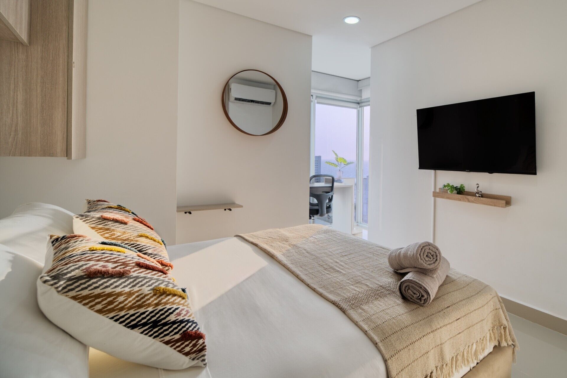 Ein modernes Schlafzimmer mit Bett, Fernseher und Blick ins Freie.