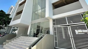A modern high-rise building with a prominent glass facade, a staircase leading to the entrance, and a metal gate with horizontal slats. - Home Beach MagnoLoft (Cartagena)