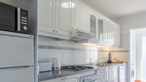 A modern kitchen with white cabinets, a built-in microwave, a stove, and a coffee maker. - Apartamento Estrela Azul (Santa Cruz)