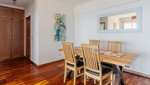 A dining area with a wooden table and chairs, a painting of a parrot, and a mirror on the wall. - Apartamento Estrela Azul (Santa Cruz)