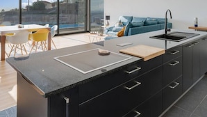 A modern kitchen with a large island, black cabinetry, and a view of the city. - Casa Mozart II 15B in Estreito da Calheta (Calheta)