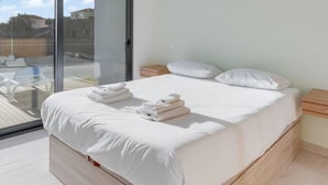 A modern bedroom with a large bed, a sliding glass door to a balcony, and a simple pendant light. - Casa Mozart II 15B in Estreito da Calheta (Calheta)
