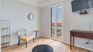 En moderne stue med sofa, rundt bord, en lille skammel, træskrivebord, fjernsyn og en skydedør med glas til altan.