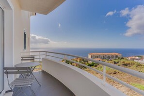 A balcony with a table and chairs, overlooking a coastal view with buildings in the distance.