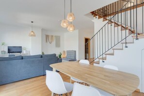 A modern living space with a wooden dining table, white chairs, a grey sofa, and a staircase with a metal railing. - Alta do Garajau I 5 W (Santa Cruz)