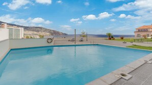 Une piscine offrant une vue dégagée sur la mer, avec un bâtiment portant l’inscription « REIDS » en arrière-plan.
