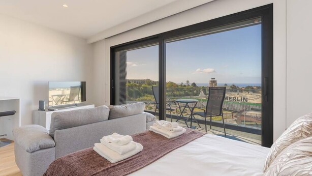 A modern hotel room with a large window, a bed, a grey sofa, and a small table with a chair. - Fenix Ocean View in Funchal (Funchal)