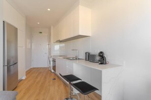 A modern kitchen with white cabinetry, a stainless steel refrigerator, a built-in oven, a sink, and two black bar stools. - Fenix Ocean View in Funchal (Funchal)