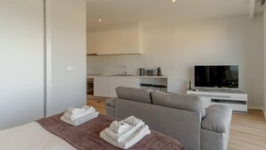 A modern hotel room with a bed, a grey sofa, a TV, and a kitchenette in the background. - Fenix Ocean View in Funchal (Funchal)
