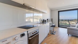 A modern kitchen with a Samsung washer, an oven, and a large window offering a view of a hilly landscape. - Fenix Ocean View in Funchal (Funchal)