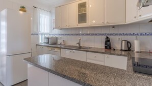 Una cocina moderna con armarios blancos, encimeras de granito, horno empotrado, cafetera y hervidor.