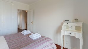 Una habitación de hotel con una cama, un tocador blanco y una puerta que da a otra habitación.