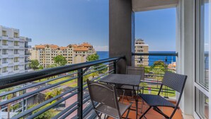 Un balcón con mesa y sillas, con vista a una zona costera con edificios y cielo despejado.