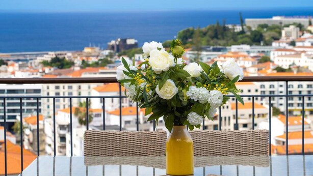A balcony with wicker furniture, a glass table, and a vase of white flowers. - Santa Luzia Funchal View 2 Bedrooms Pool (Funchal)