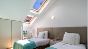 A bedroom with two beds, a skylight, a bedside table with a lamp, and a view of the outside. - Santa Luzia Funchal View 2 Bedrooms Pool (Funchal)